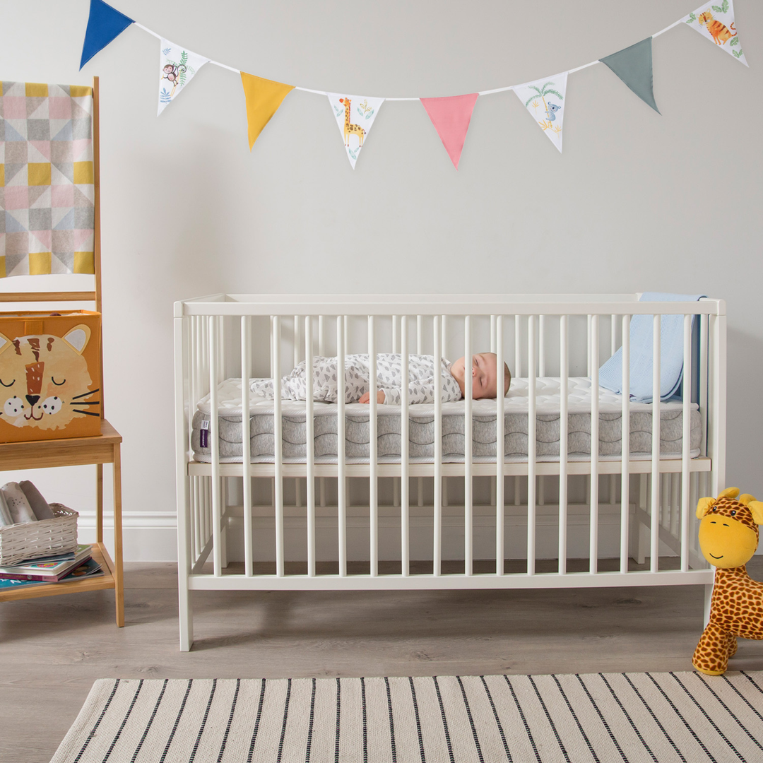 Modern white baby cot with a sleeping infant in a bright, stylish nursery featuring a neutral colour palette, wooden furniture, playful bunting, and soft toys — ideal inspiration for baby room décor or sustainable nursery design.