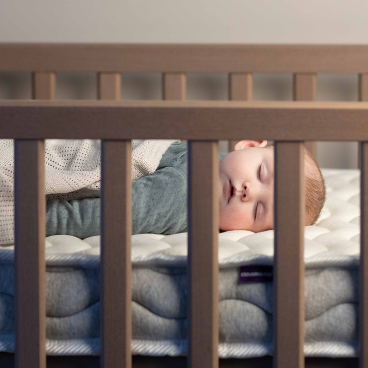 Baby sleeping soundly on ClevaMama ClevaFoam Deluxe Pocket Sprung Mattress in a wooden cot — premium breathable and supportive baby mattress designed for ultimate comfort, pressure relief, and safe infant sleep.