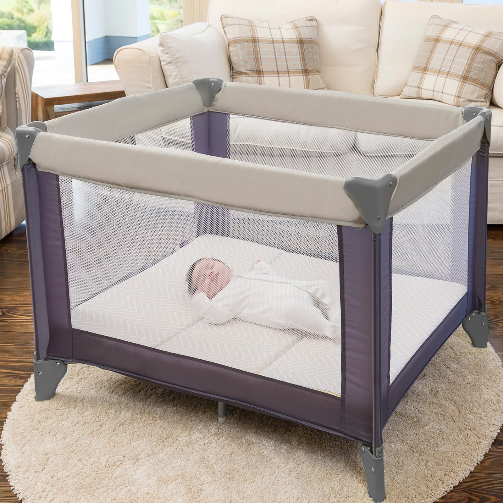 Baby in a purple and gray playpen with ClevaMama mattress in a living room setting.