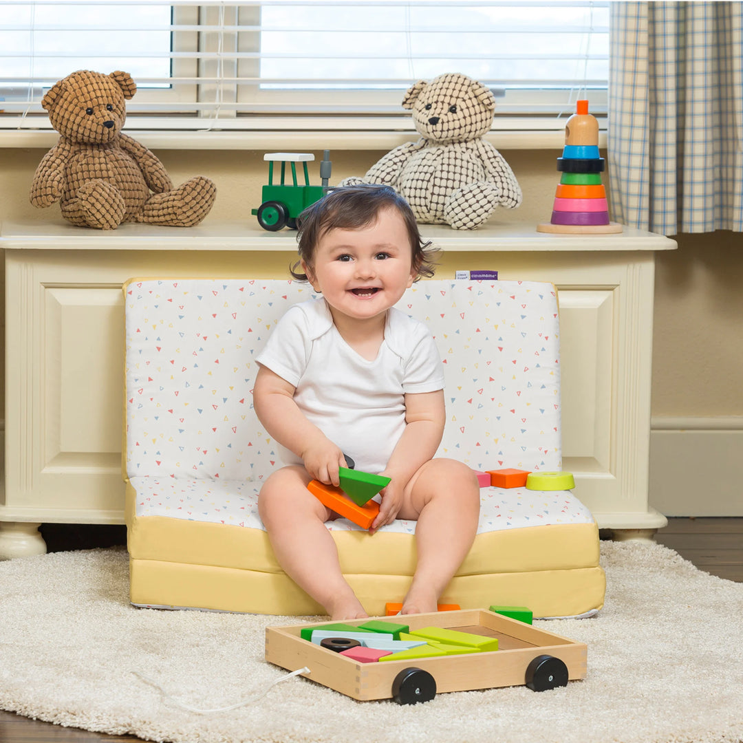 Child sitting on the ClevaMama travel mattress in seat mode in a playroom.