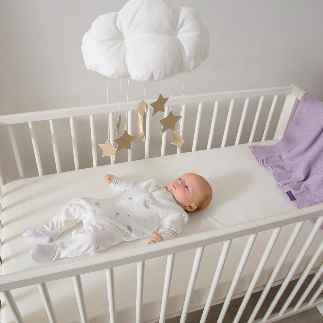 Baby lying safely on Clevamama Waterproof Support Mattress in white cot, featuring hypoallergenic, breathable, and durable foam for ultimate comfort and support. Premium waterproof baby cot mattress designed for newborns and infants, asthma and allergy certified, ensuring a safe, hygienic, and restful sleep environment.