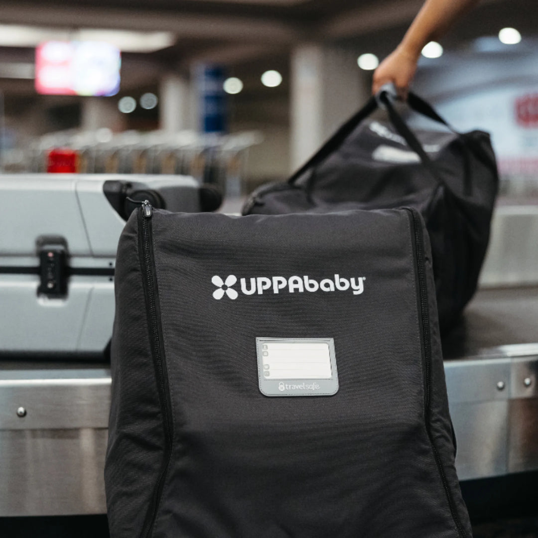 UPPAbaby MESA i-Size car seat travel bag on an airport baggage belt with TravelSafe ID window.
