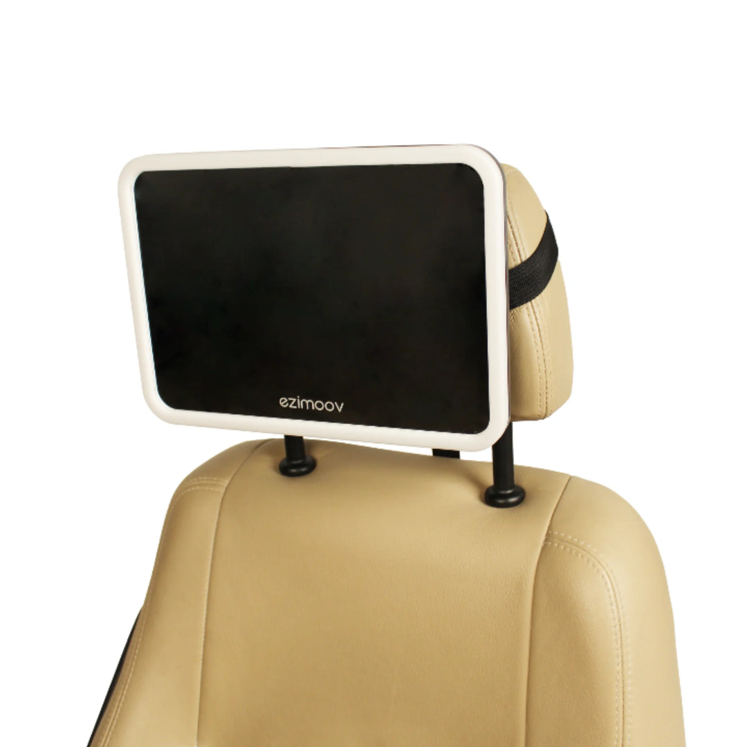 EziMoov LED Pro baby car seat mirror mounted on a beige car headrest, showing its large rectangular design and secure strap attachment for clear rear-facing baby visibility.