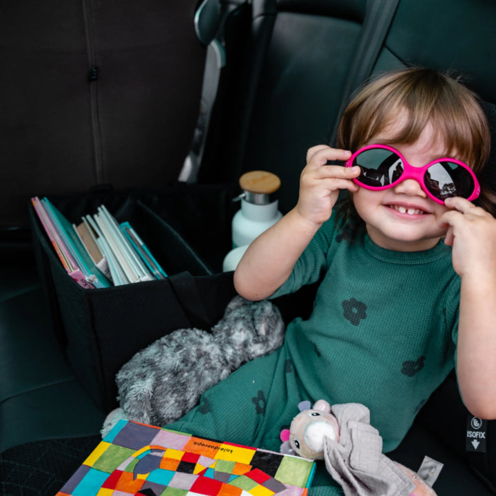 Child in car seat with Ezimoov car storage organiser holding books, bottle and toys