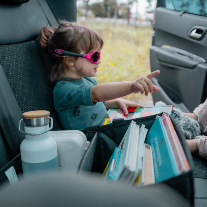 Child in back seat with Ezimoov car storage organiser holding books and bottle for travel