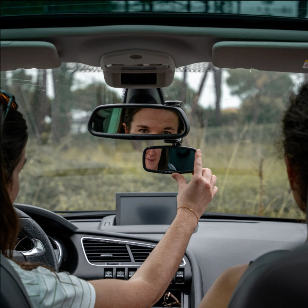 Parent adjusting the Ezimooov clip-on rear-view baby mirror inside a car, showing how the adjustable mirror attaches below the main rear-view mirror to improve visibility of children in the back seat.