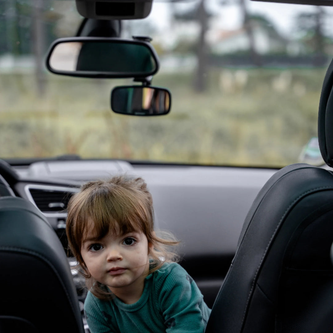 Child sitting in the back seat of a car with the Ezimooov clip-on rear-view baby mirror visible on the main mirror, showing how the adjustable mirror helps parents monitor kids while driving.