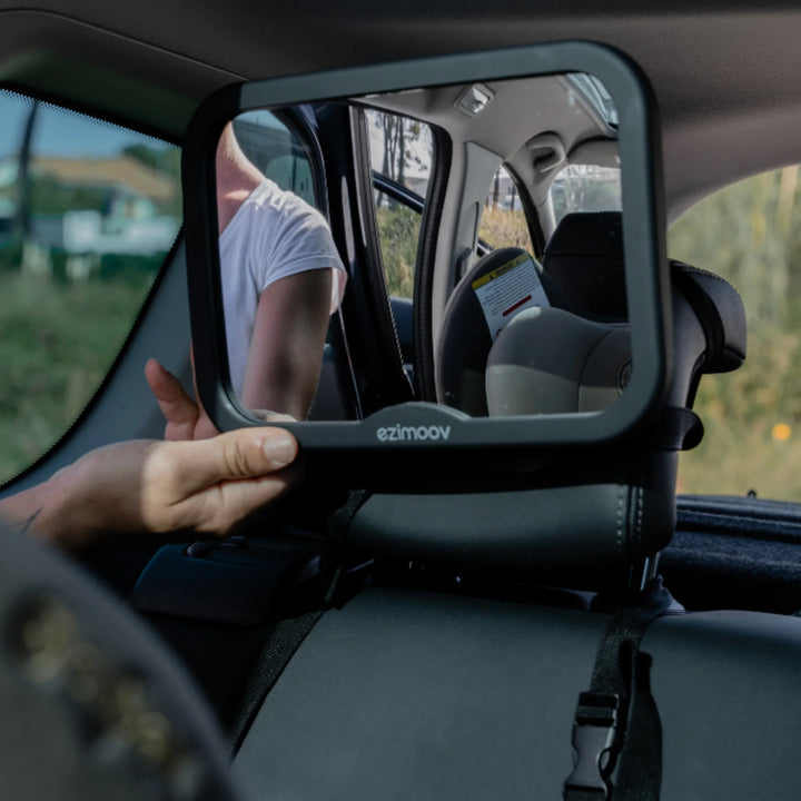 Parent adjusting Ezimoov large baby car seat mirror on rear headrest to improve visibility of child in back seat for safer driving.