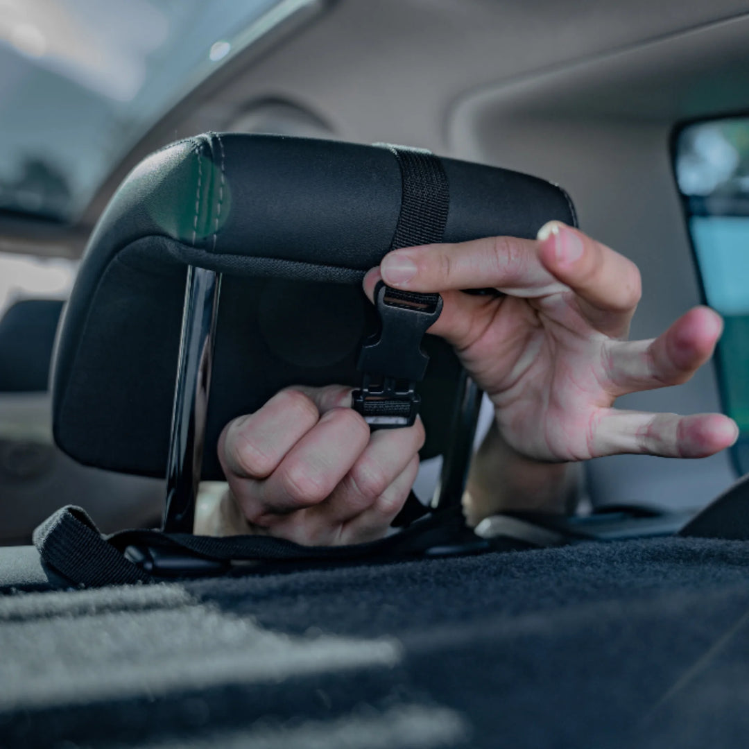 Close-up of a parent fastening the adjustable strap of an EziMoov rear-facing baby car seat mirror to a car headrest, demonstrating simple and secure installation for safer infant monitoring while driving.