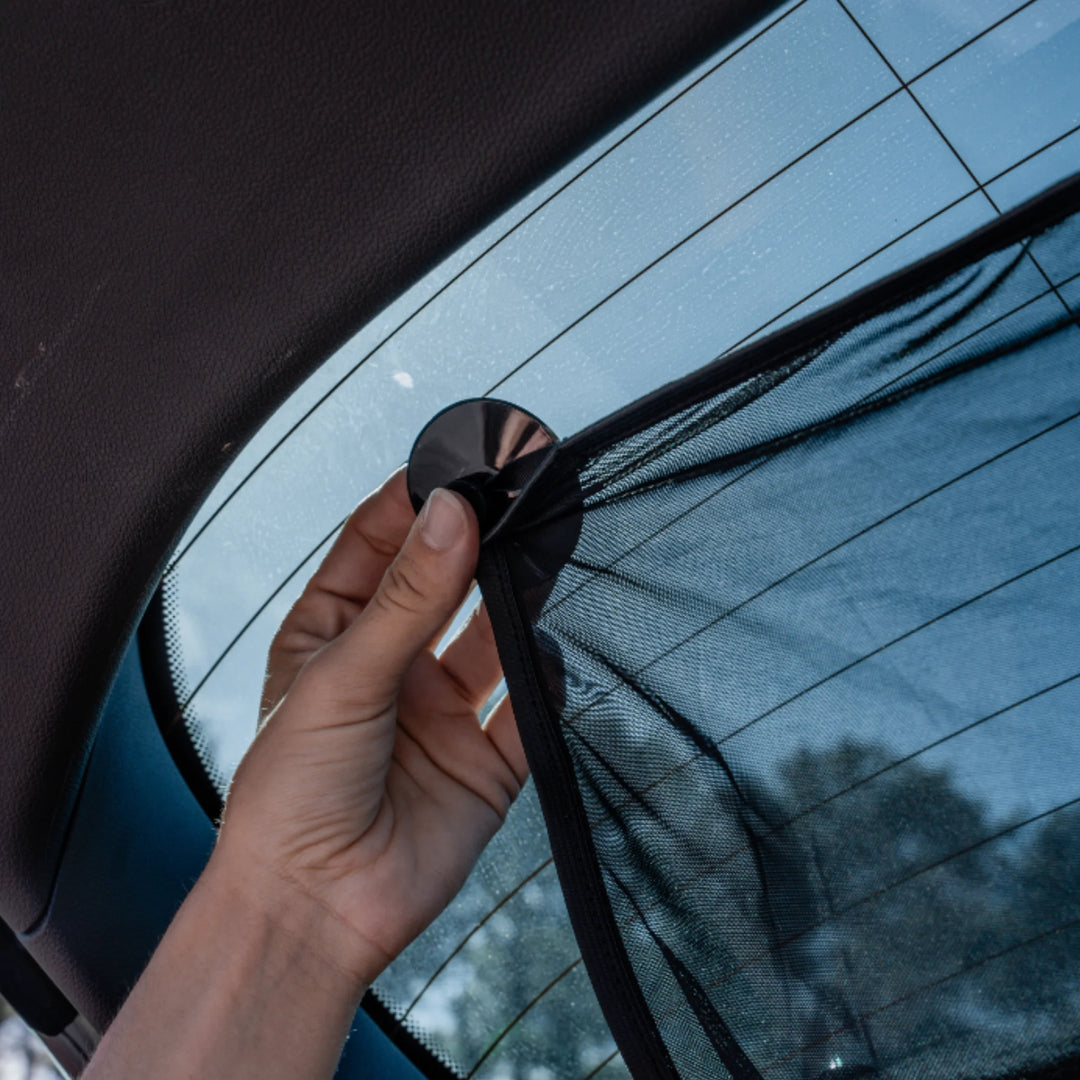 Hand pressing suction cup to attach the EziMoov rear windscreen sunshade to the back window, demonstrating quick and secure installation of the UV-blocking mesh sun shield for car rear windows.