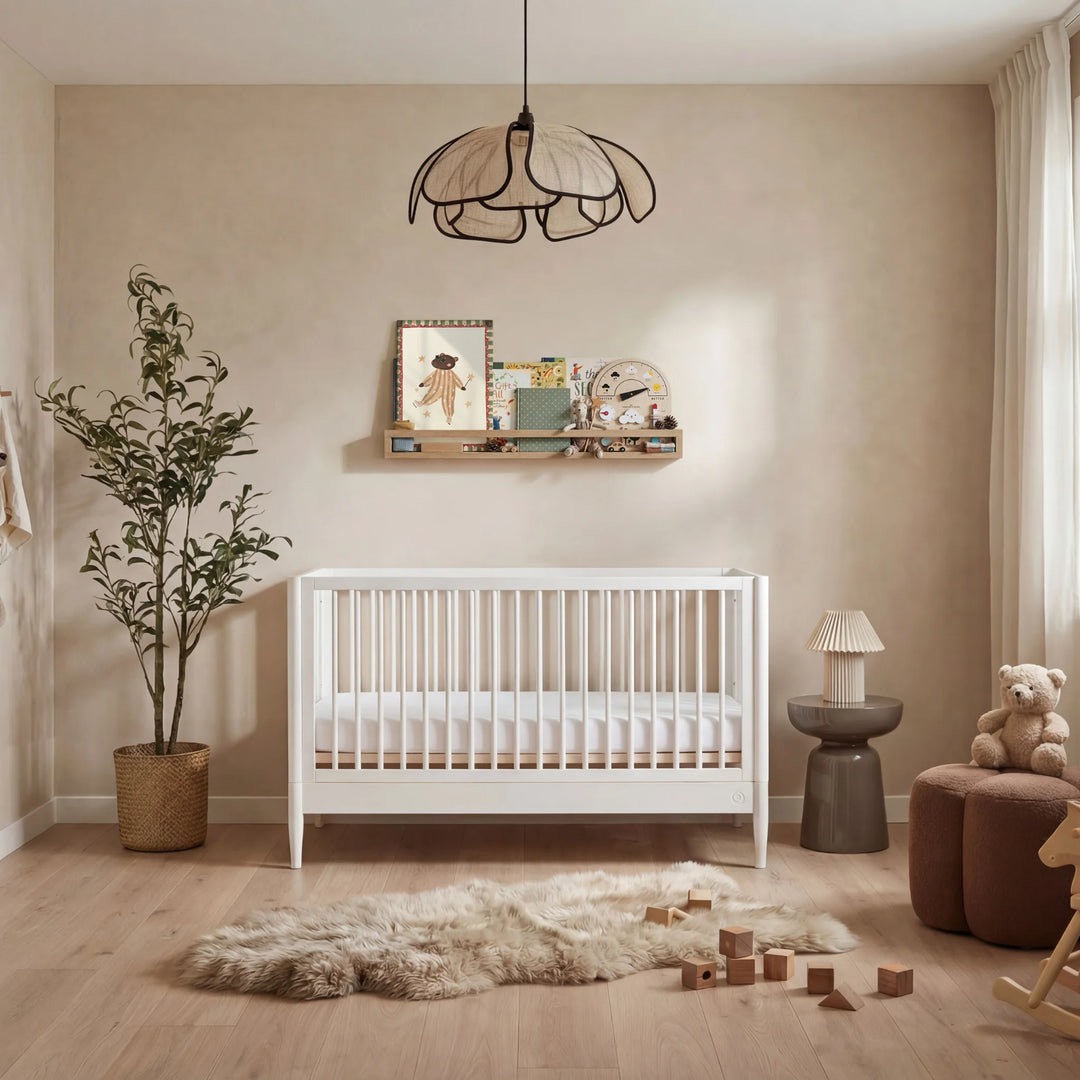 Gaia Baby Eos convertible cot bed in white styled in a warm neutral nursery with wooden floor, soft rug, and decorative shelving