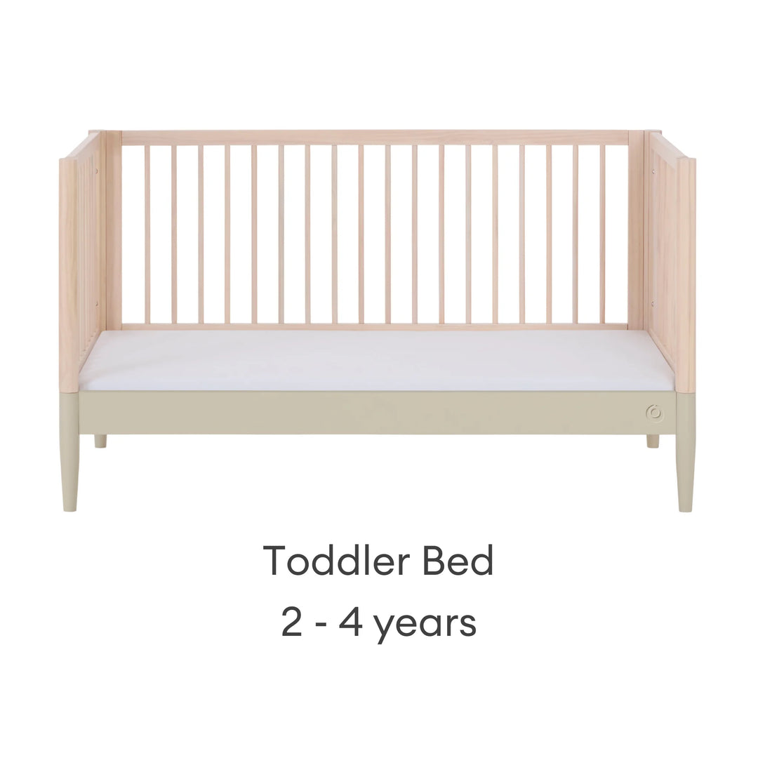 Gaia Baby Eos convertible cot transformed into toddler bed for ages 2–4 years in natural desert sage finish on a white background.