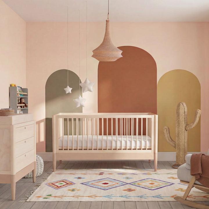 Gaia Baby Eos convertible cot in natural wood with powder blush nursery styling, featuring colourful wall arches, dresser and modern decor.