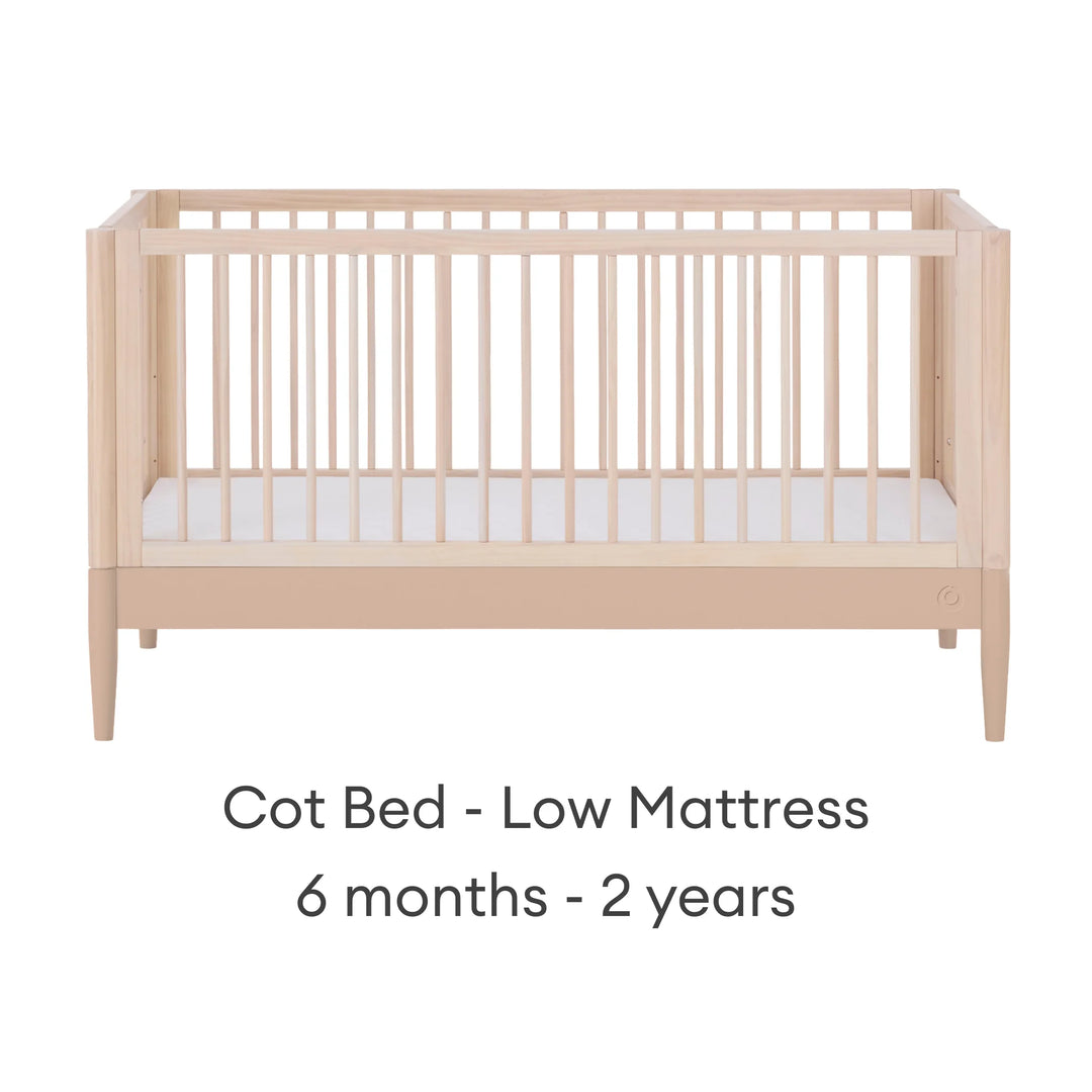 Gaia Baby Eos convertible cot in natural wood and powder blush finish with mattress in low position for 6 months to 2 years on a white background.