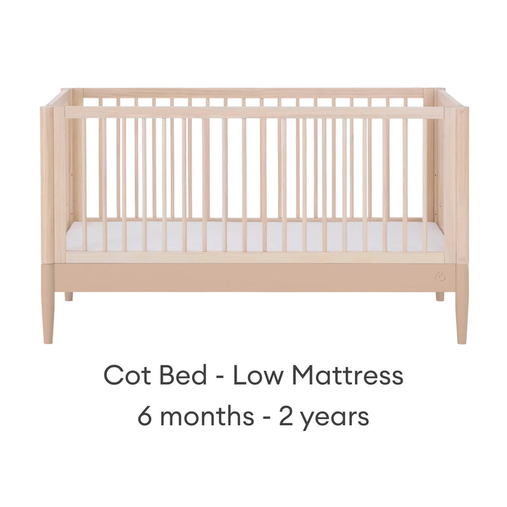 Gaia Baby Eos convertible cot in natural wood and powder blush finish with mattress in low position for 6 months to 2 years on a white background.