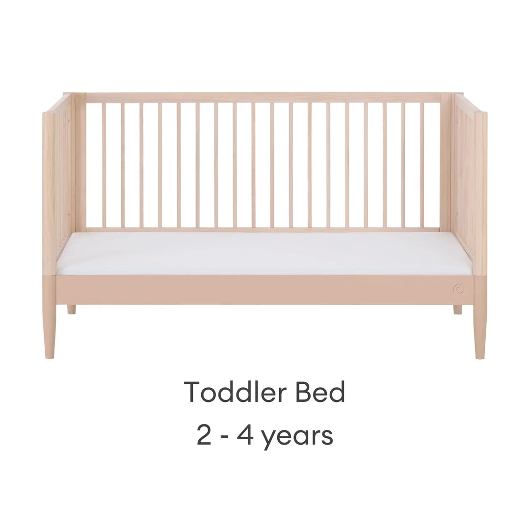 Gaia Baby Eos convertible cot transformed into toddler bed in natural wood and powder blush finish for ages 2–4 years on a white background.