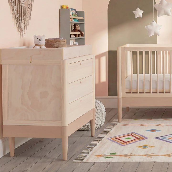 Gaia Baby Eos dresser in natural wood and powder blush in a nursery with matching crib