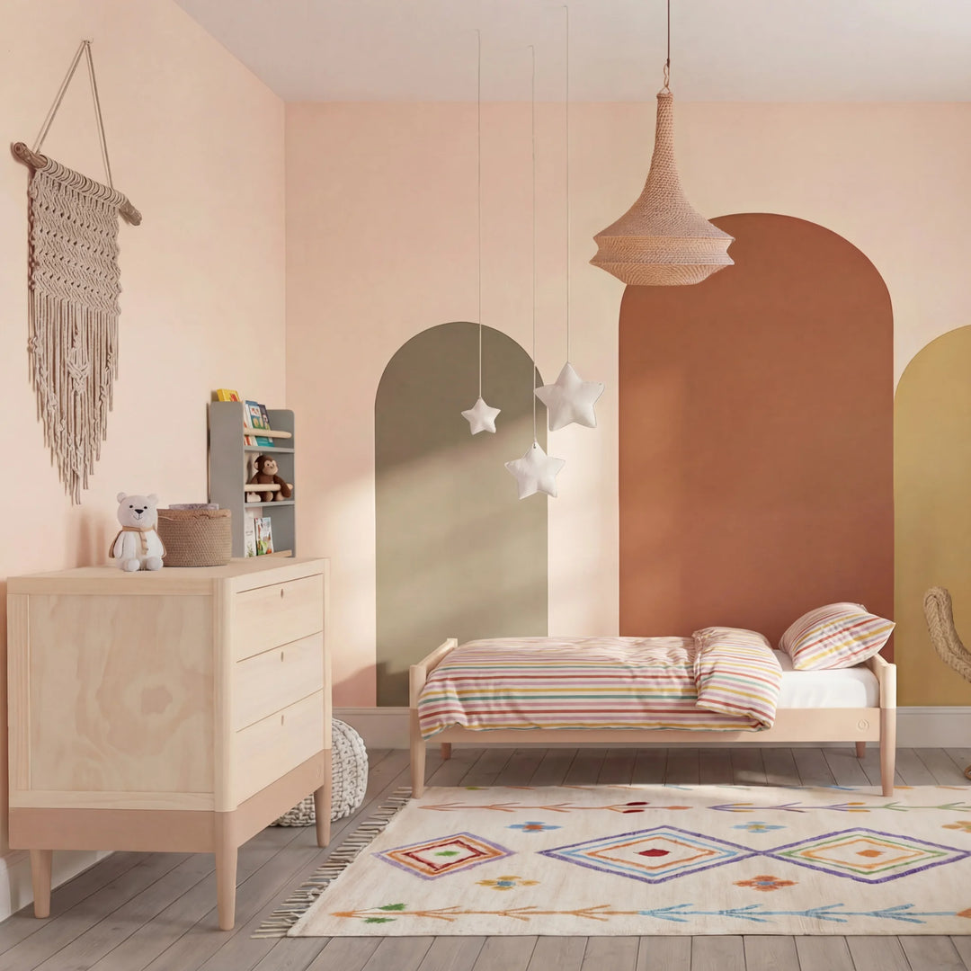 “Gaia Baby Eos toddler bed and dresser in natural wood styled in blush nursery with arched wall and warm tones”