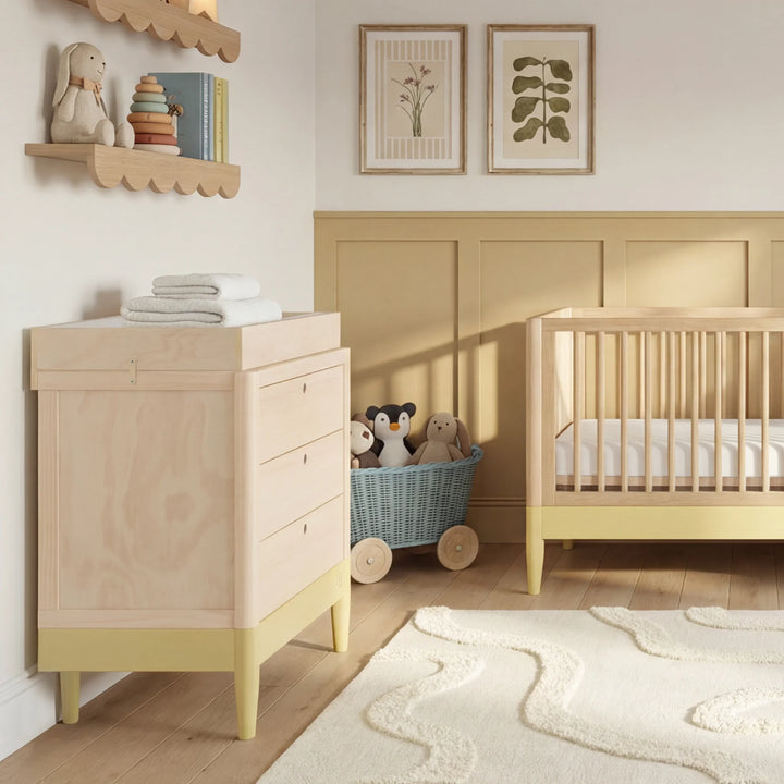 Gaia Baby Eos dresser with changer in natural wood and primrose yellow in a nursery with crib