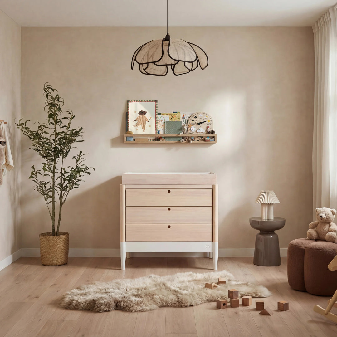 Gaia Baby Eos dresser in natural wood and white in a neutral nursery with soft lighting and wooden toys.