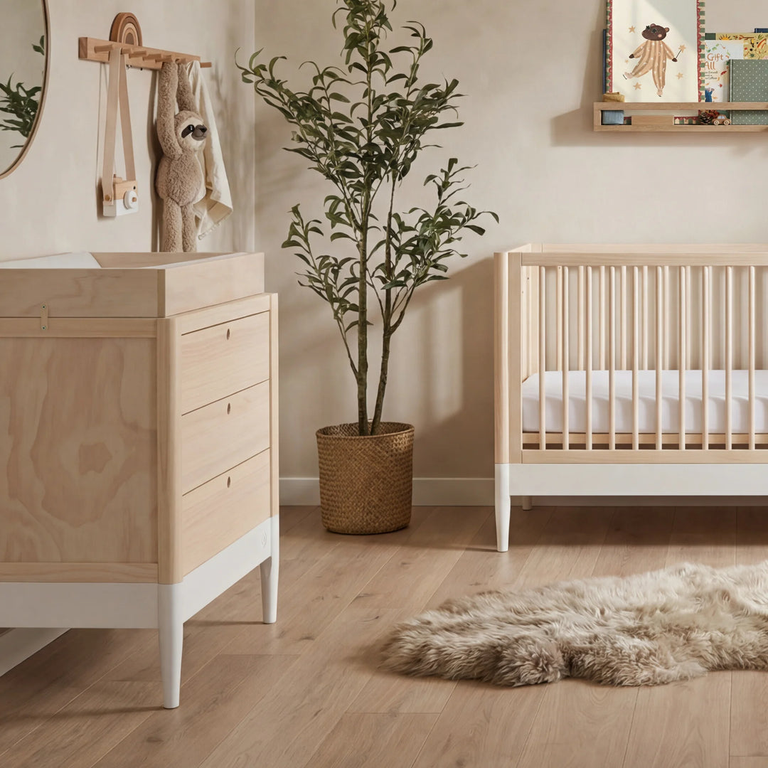 Gaia Baby Eos dresser in natural wood and white beside matching cot in a neutral nursery setting