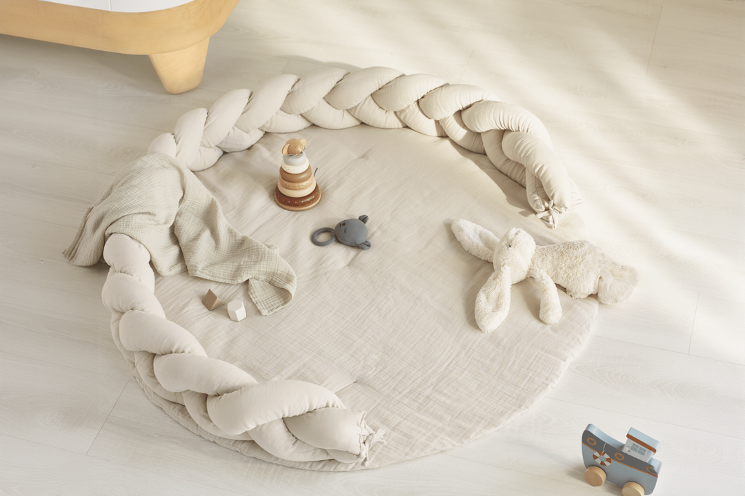 This image showcases the super soft muslin 100% organic cotton play mat from Gaia Baby with the braided pillow nursery accessory being used as a border to be a cosy tummy time area for your little one.