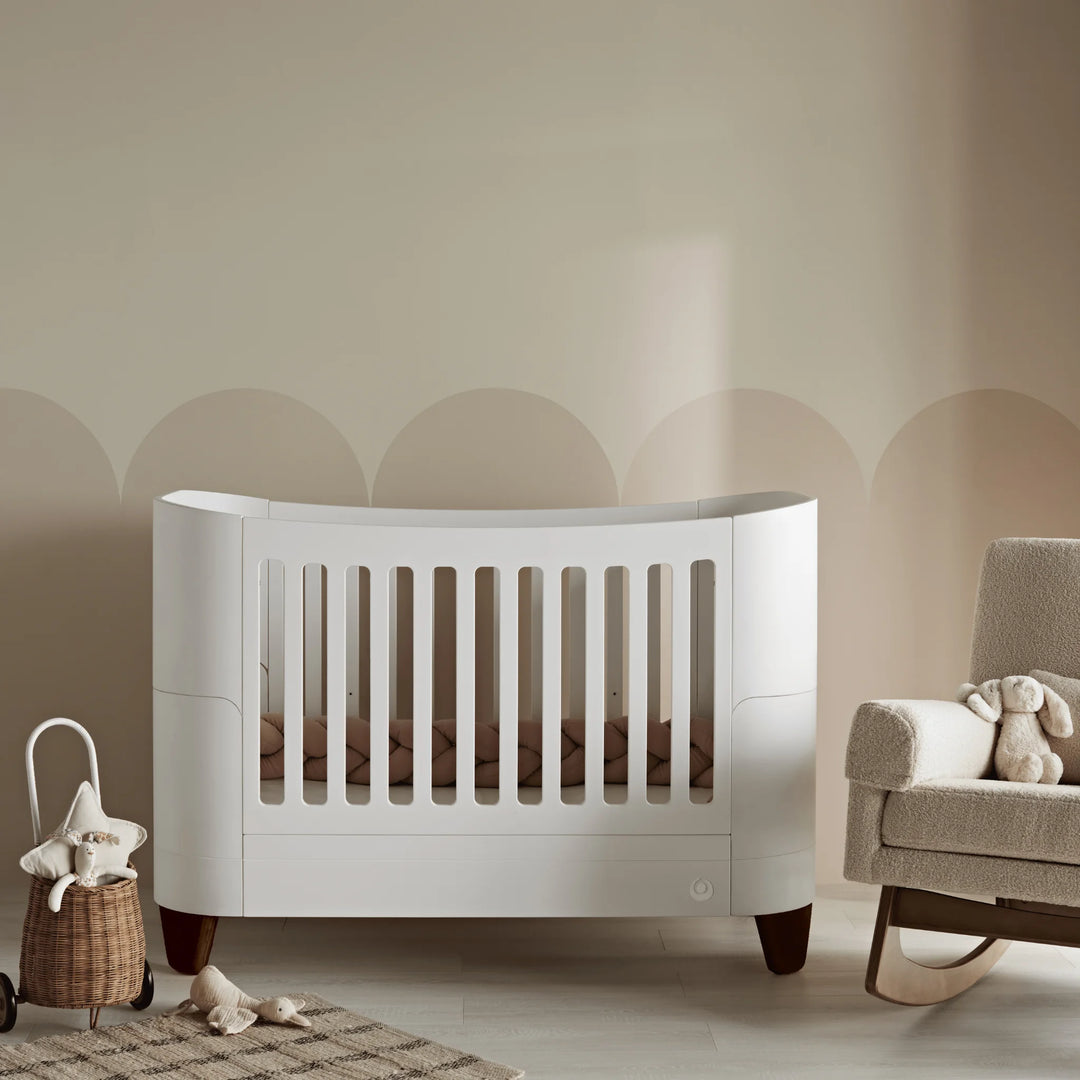 Serena white cot bed with walnut wood legs in neutral nursery with Serena biscuit boucle rocking chair.