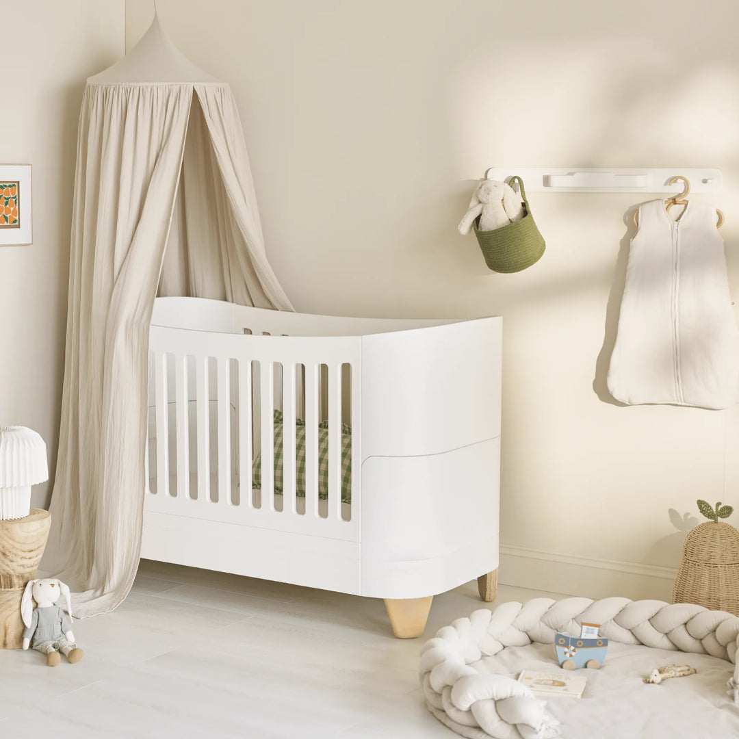 Serena real wood cot in nursery with organic cotton muslin canopy and soft furnishings.
