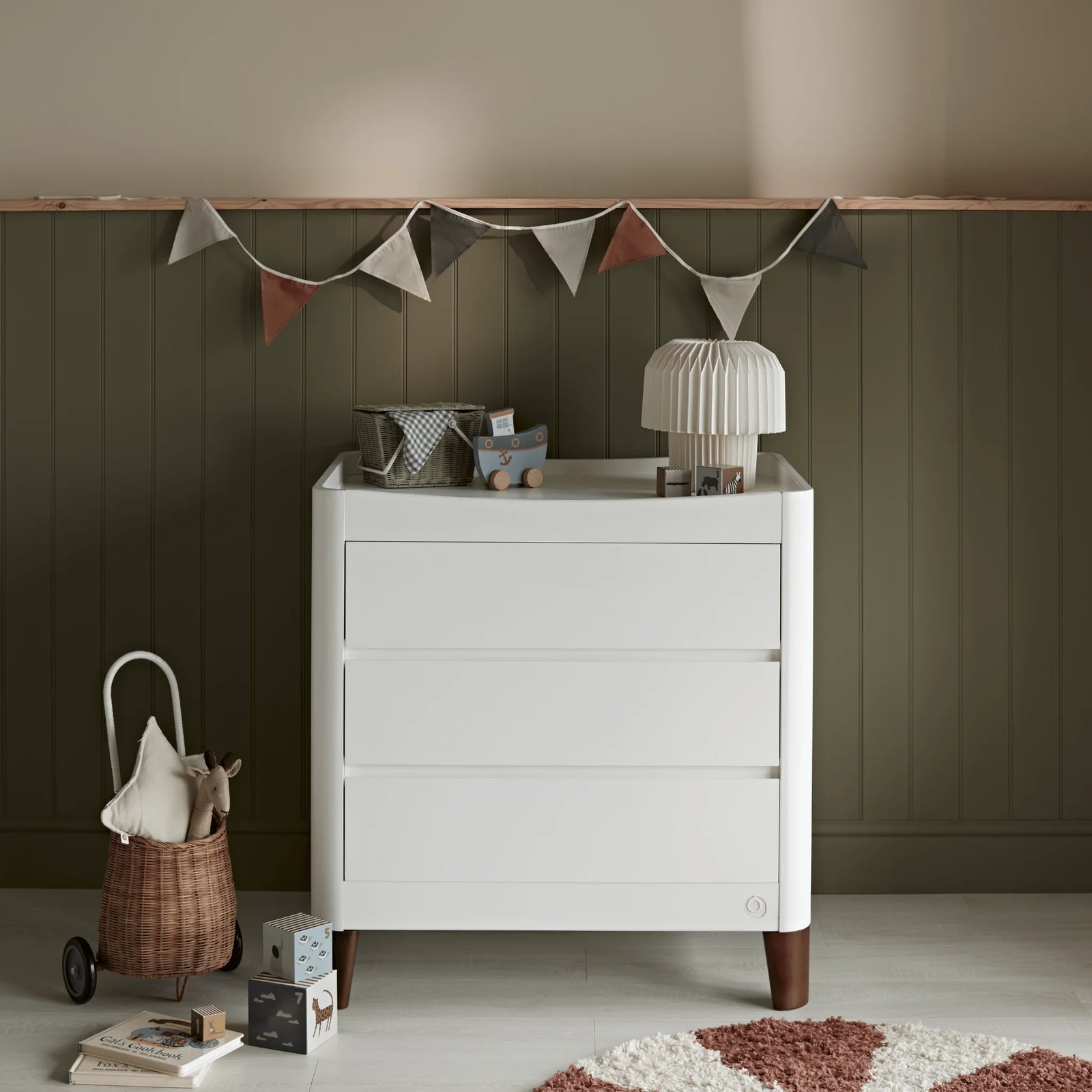 Gaia Baby Serena dresser in white with walnut legs styled in a nursery against a green panelled wall