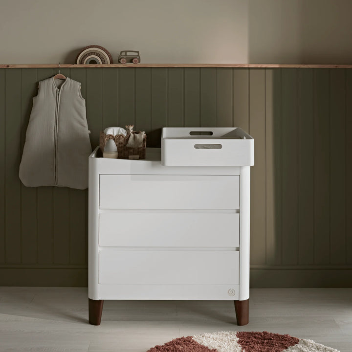 Gaia Baby Serena white dresser with walnut legs and Hera changing station styled in a nursery with a green panelled wall