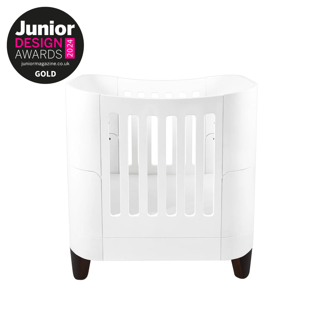 Serena Small Cot Bed with Walnut Legs and Gold Junior Design Awards 2024 logo.