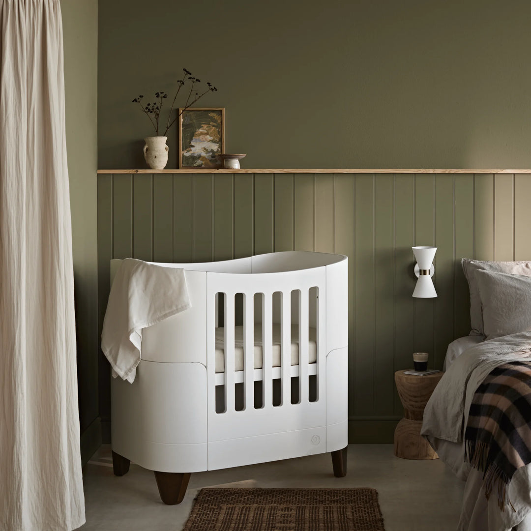 Serena mini cot with walnut legs beside parents bed.