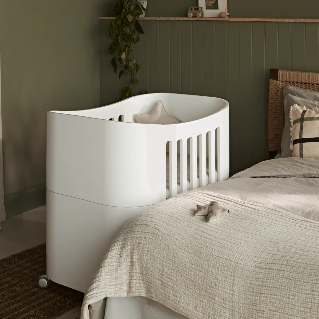Compact baby cot with wheels in parents room, next to parents bed.