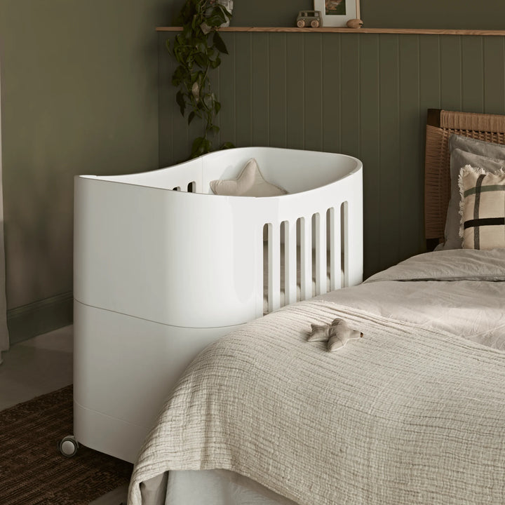 Compact baby cot with wheels in parents room, next to parents bed.