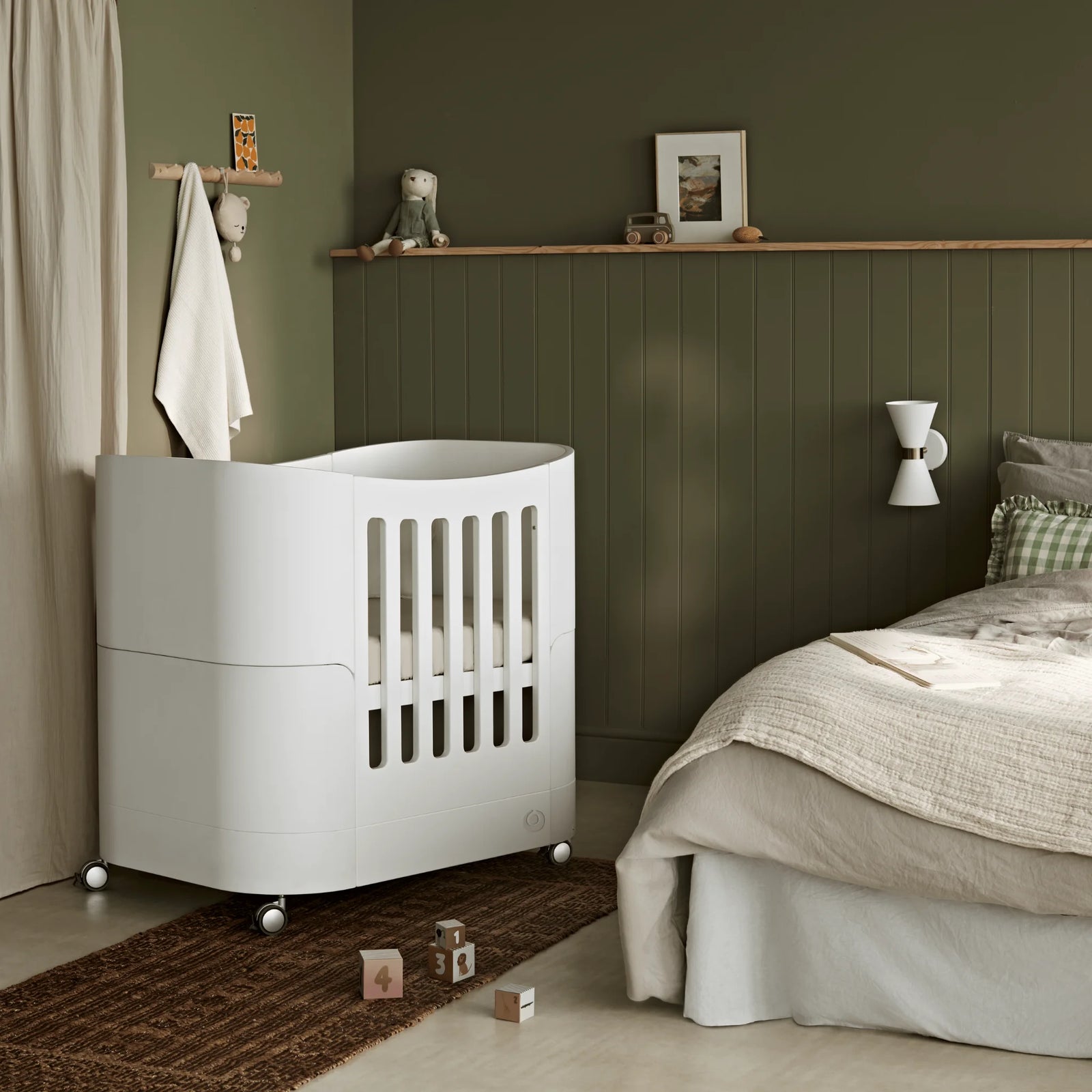 Compact baby cot with wheels in parents room, away from bed.