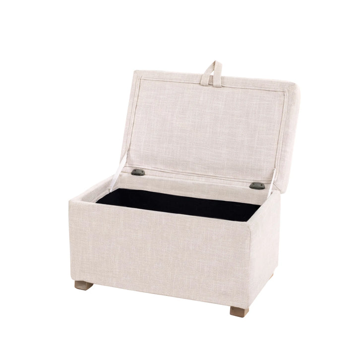 The Gaia Baby Serena Footstool in oat fabric shown at an angled view with the lid open on a white background, featuring a soft upholstered storage ottoman with a spacious interior compartment and light wooden feet.