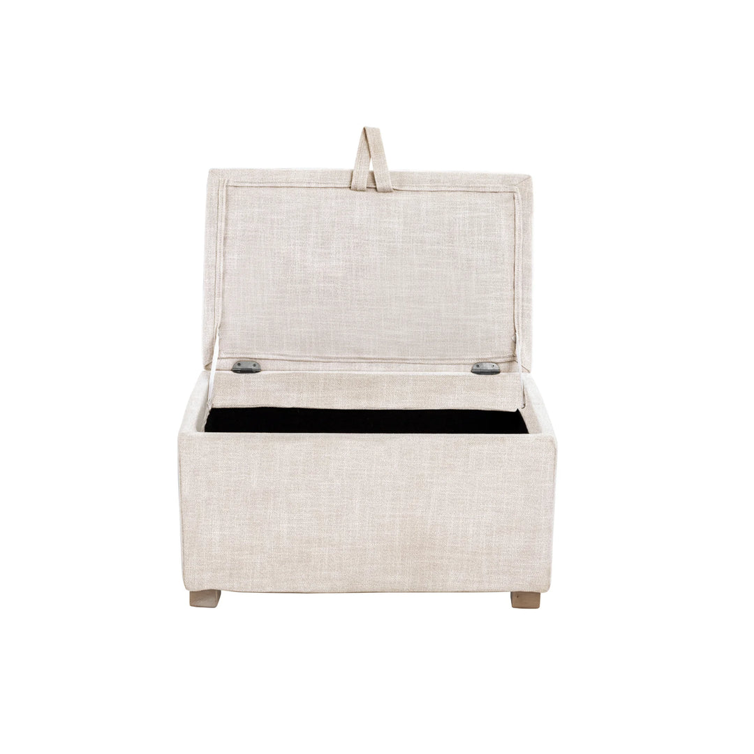 The Gaia Baby Serena Footstool in oat fabric shown from the front with the lid open on a white background, featuring a soft upholstered storage ottoman with a spacious interior compartment and light wooden feet.