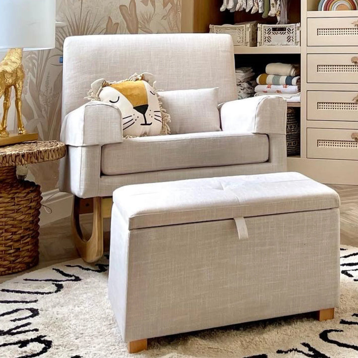A cozy nursery scene featuring the Gaia Baby Serena rocking nursing chair and matching storage footstool in soft oat fabric, styled with decorative cushions, shelving, and warm nursery décor.