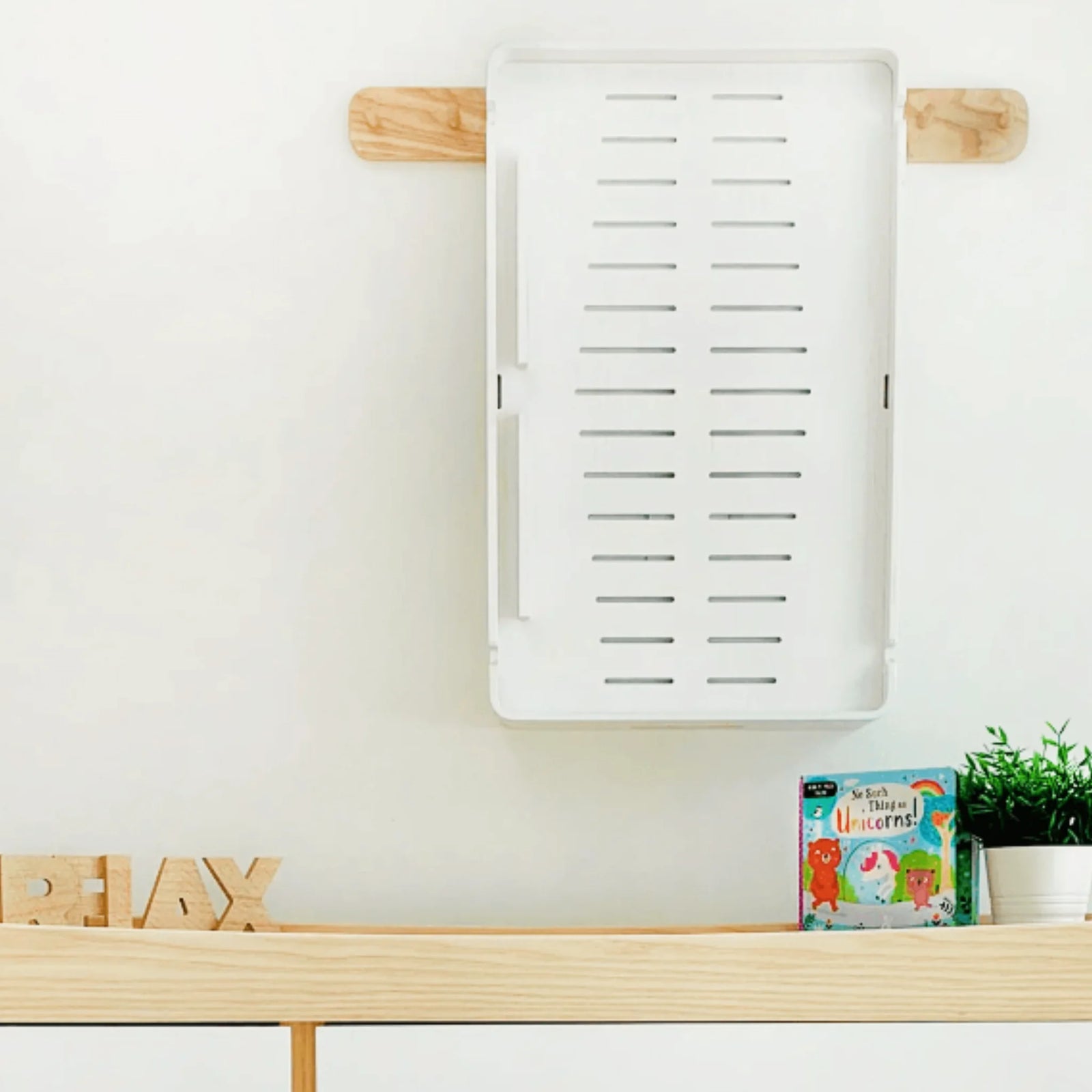 Gaia Baby Hera white changing station mounted on a nursery wall, showing underside ventilation design and compact storage capability above a wooden shelf with toys and décor.