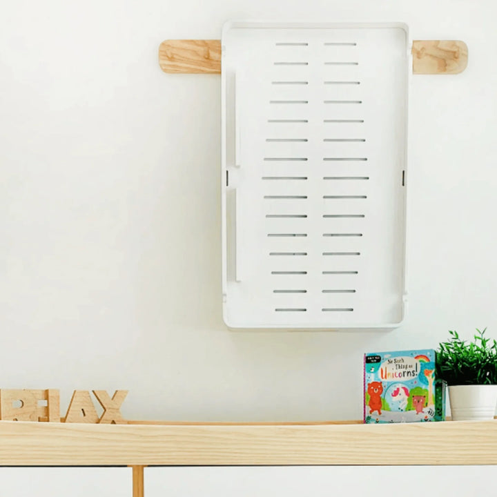 Gaia Baby Hera white changing station mounted on a nursery wall, showing underside ventilation design and compact storage capability above a wooden shelf with toys and décor.