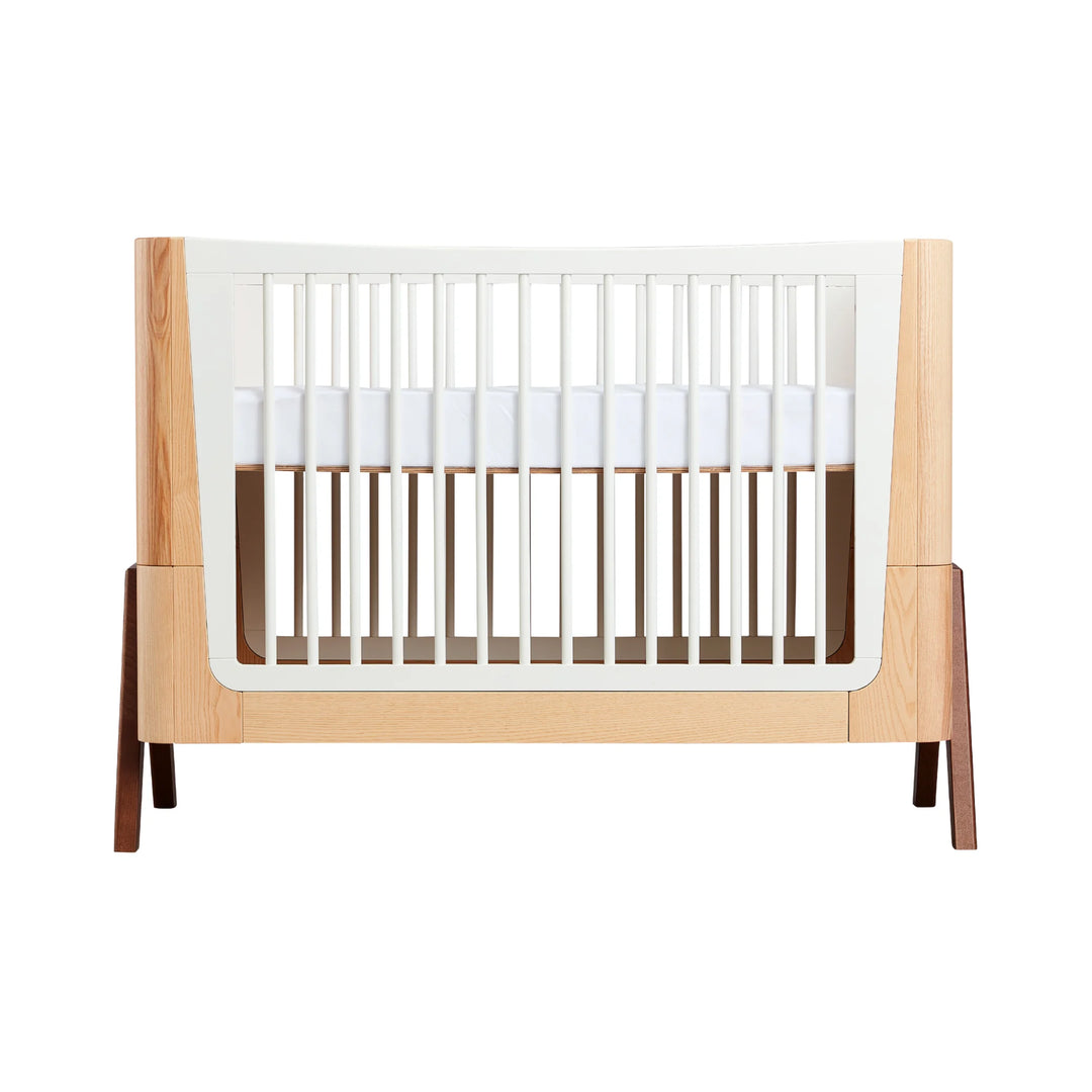 Gaia Baby Hera cot in ash and walnut, featuring Scandinavian curved design, natural wood frame, white slatted sides and modern A-frame legs — premium sustainable baby crib.
