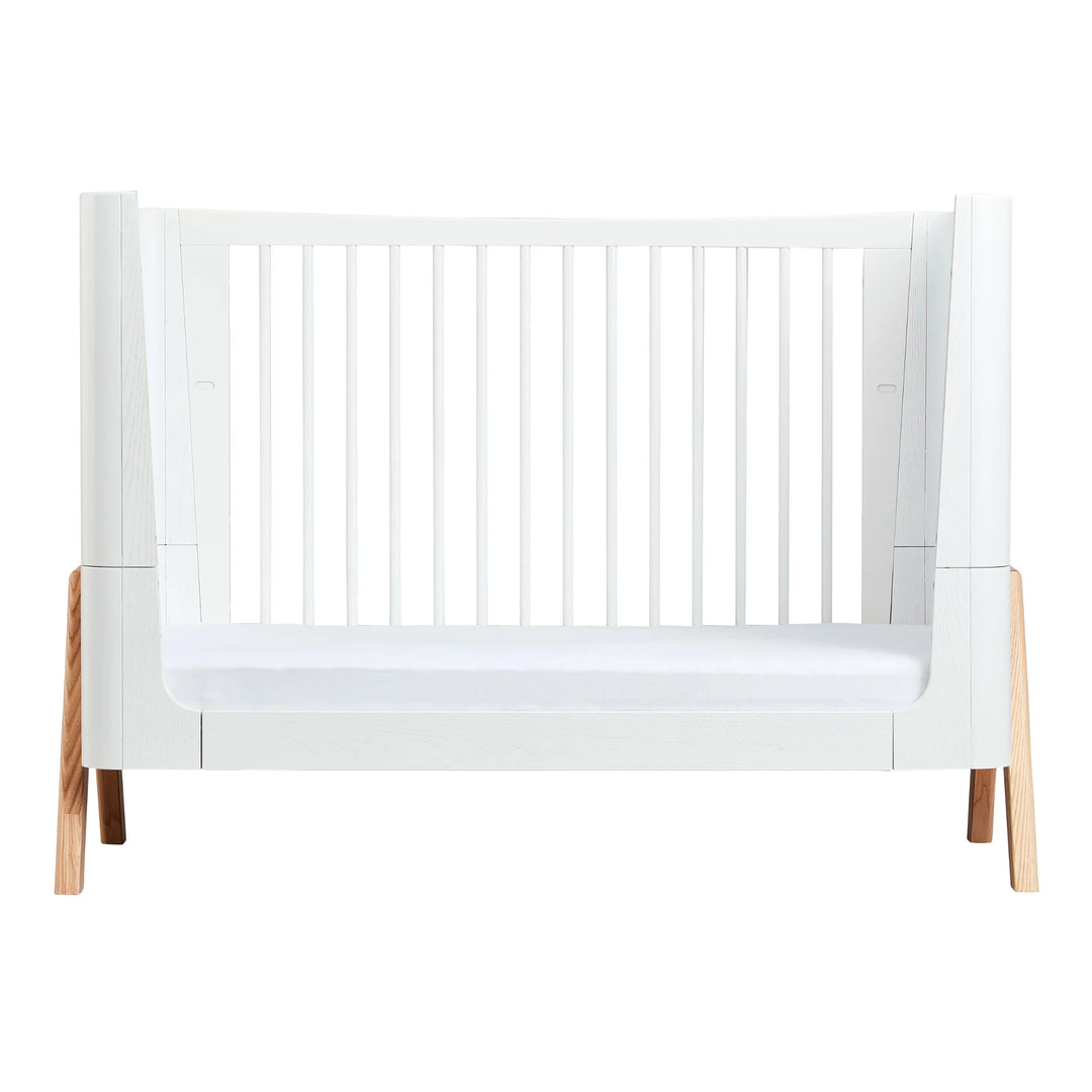 Gaia Baby Hera cot bed in Scandi White and natural wood, shown in toddler bed mode with white slatted sides, curved Scandinavian design and solid natural A-frame legs — premium sustainable convertible nursery furniture.