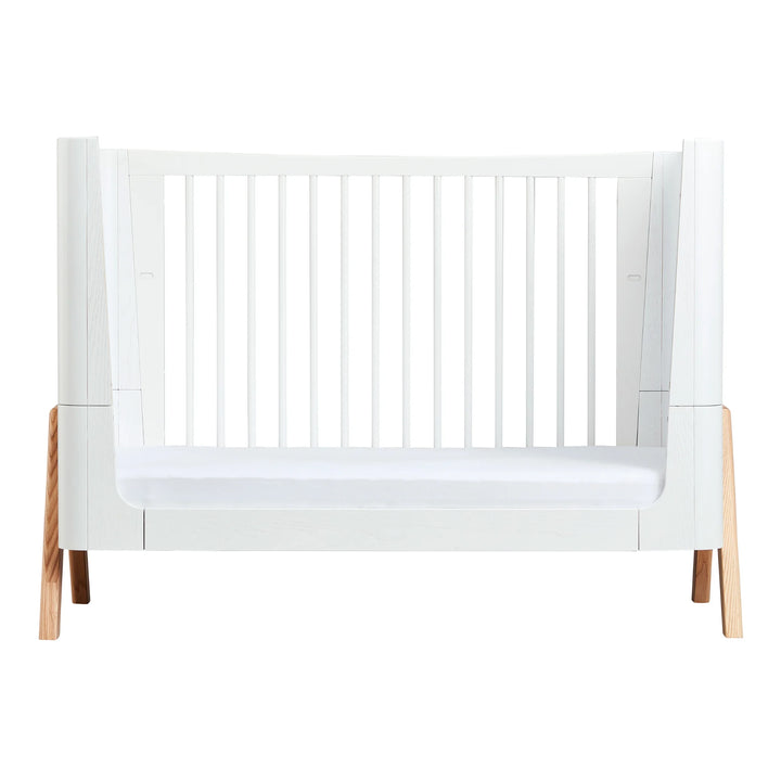 Gaia Baby Hera cot bed in Scandi White and natural wood, shown in toddler bed mode with white slatted sides, curved Scandinavian design and solid natural A-frame legs — premium sustainable convertible nursery furniture.
