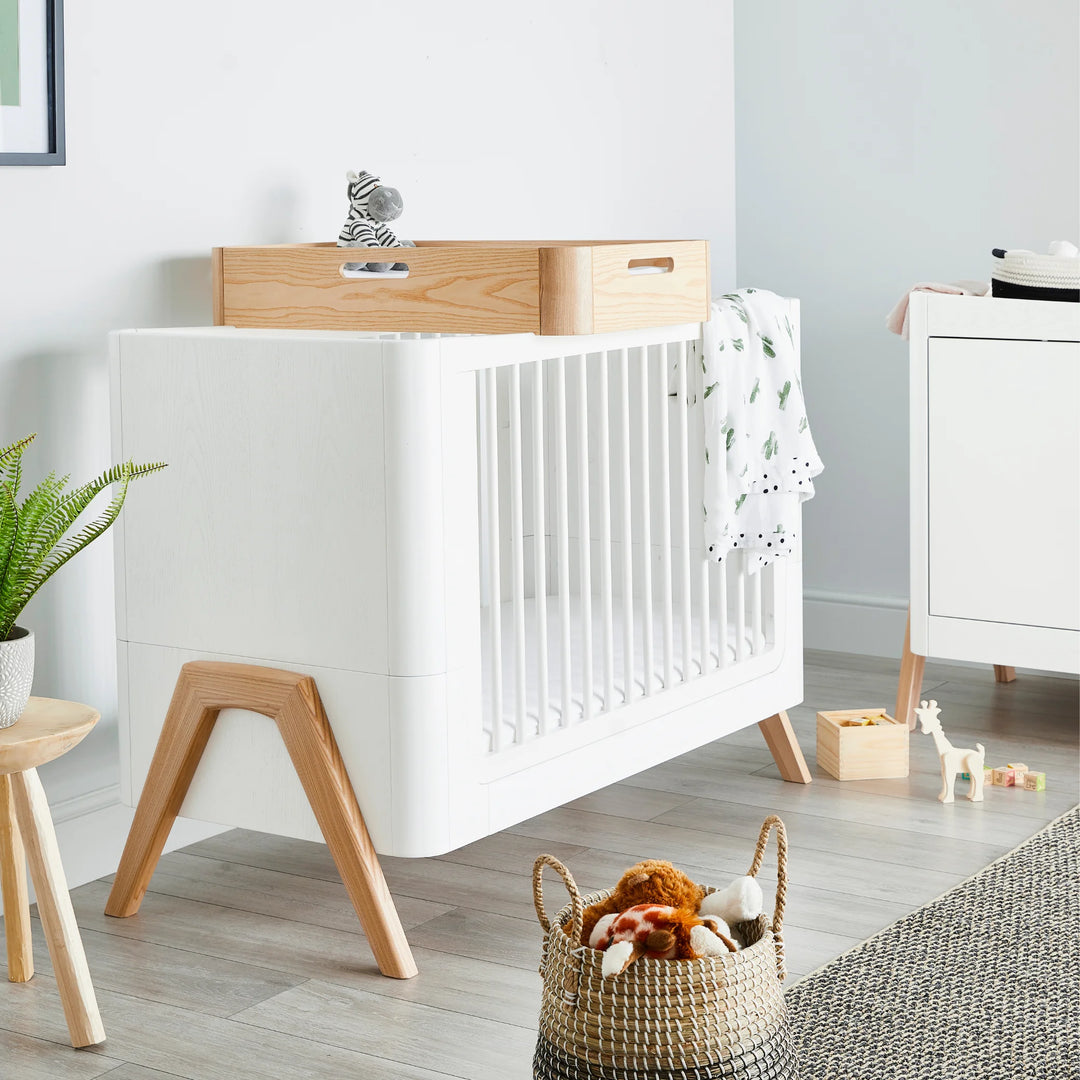 Scandinavian-style nursery featuring the Gaia Baby Hera cot bed in Scandi White with natural wood legs, styled with soft neutral décor, toys and plants — modern sustainable baby furniture in a contemporary room setting.