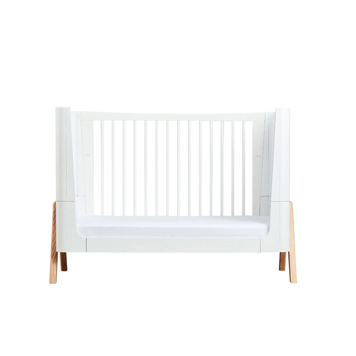 Gaia Baby Hera Cot in Natural Scandi White shown in toddler bed mode, featuring modern white frame, natural wood legs, open side design and minimalist Scandinavian styling; premium eco-friendly cot bed for contemporary nursery interiors.