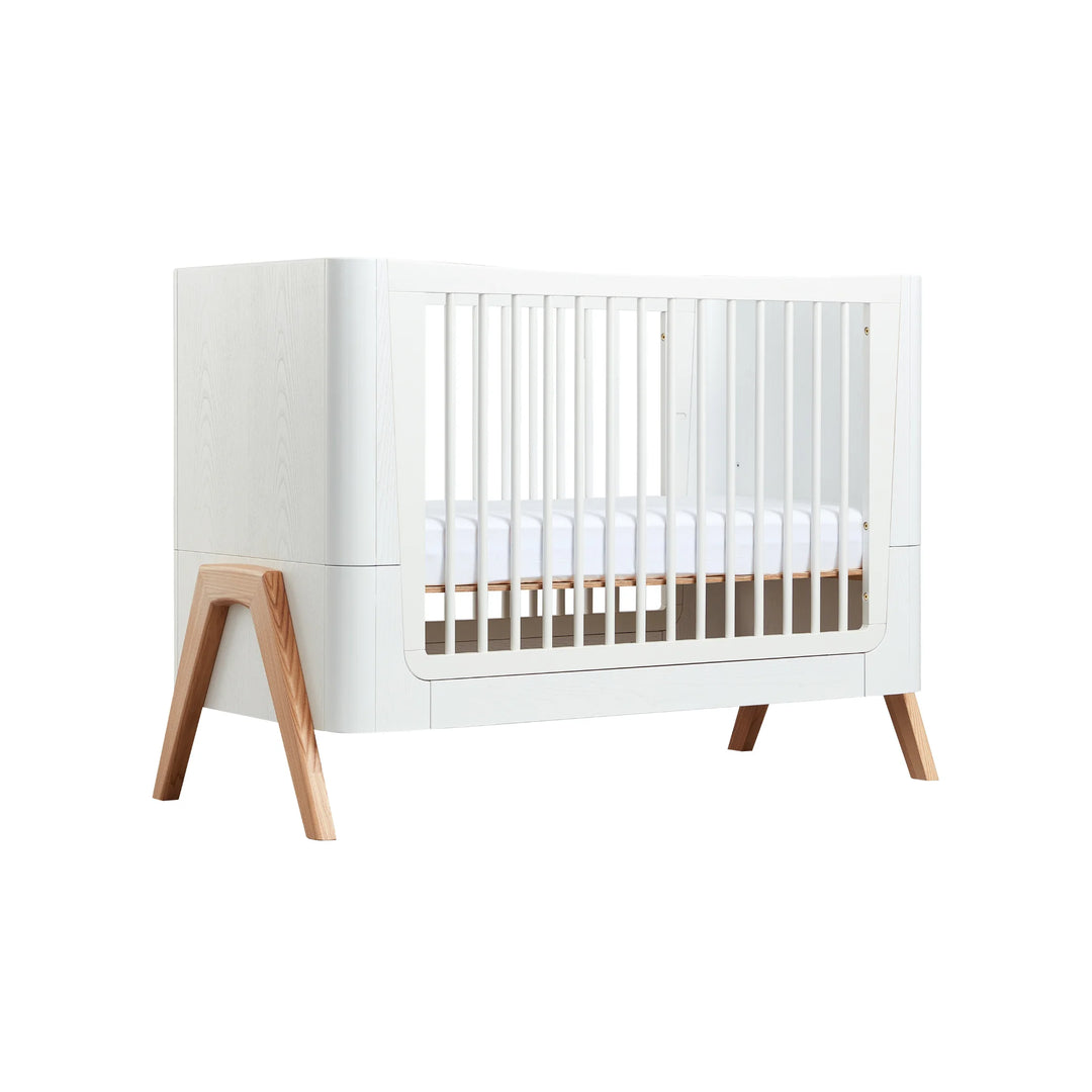 Front view of the Gaia Baby Hera Cot in Natural Scandi White, showcasing its modern white frame, natural wood legs, and safe slatted sides; premium eco-friendly Scandinavian-style cot bed for contemporary nursery design.