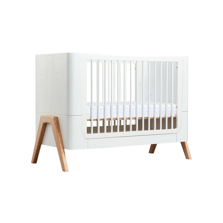 Front view of the Gaia Baby Hera Cot in Natural Scandi White, showcasing its modern white frame, natural wood legs, and safe slatted sides; premium eco-friendly Scandinavian-style cot bed for contemporary nursery design.