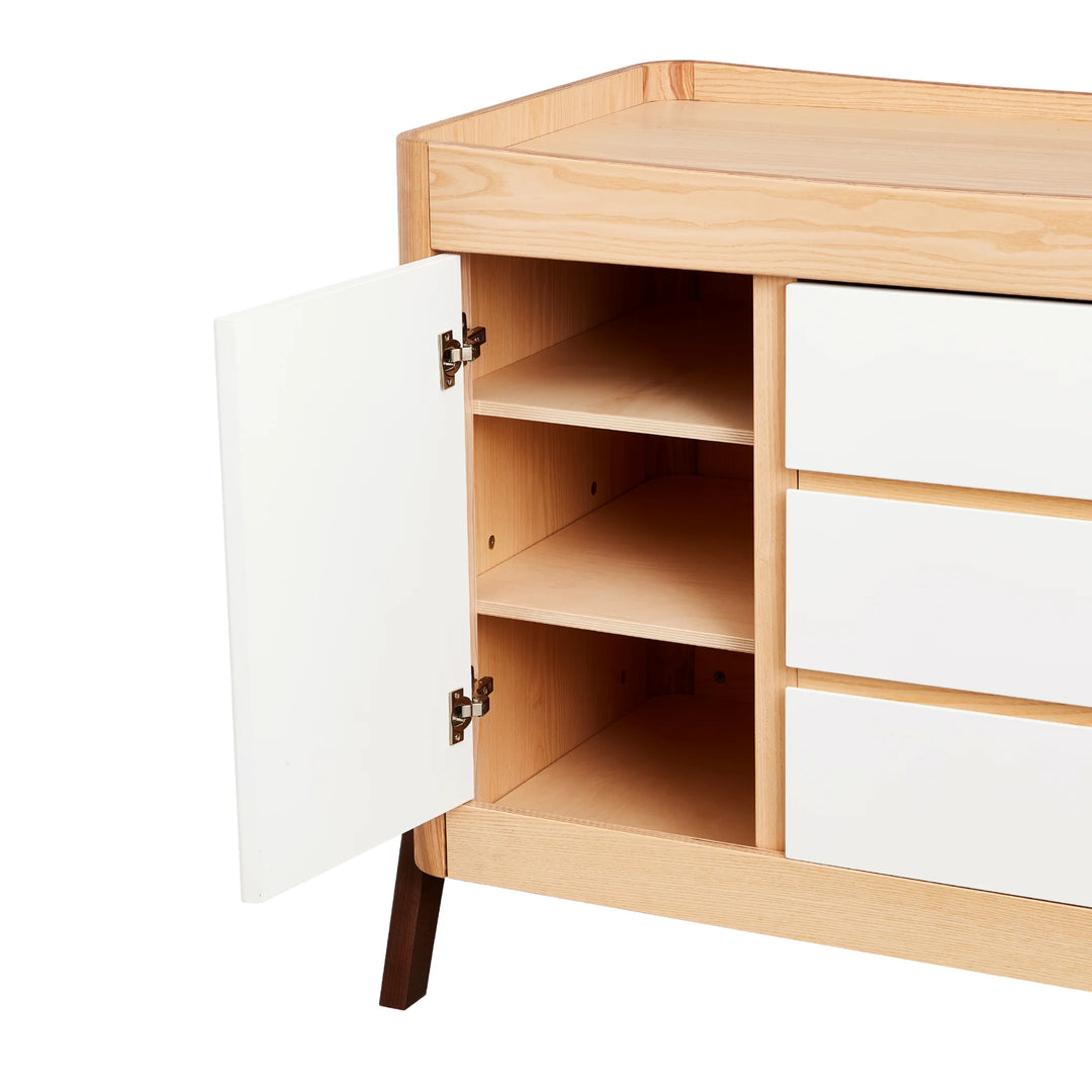 Gaia Baby Hera dresser in ash and walnut with open cabinet door showing adjustable interior shelving and three smooth white drawers — premium Scandinavian nursery storage furniture.