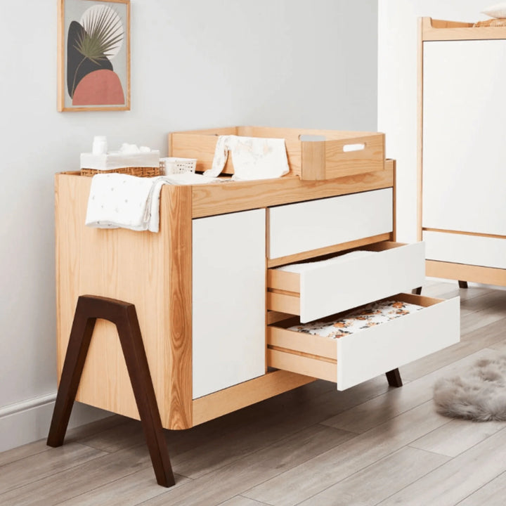 Gaia Baby Hera dresser in Scandi white and natural ash with walnut legs shown in a modern nursery, featuring open drawers, changing tray and baby essentials displayed in a Scandinavian design setting.