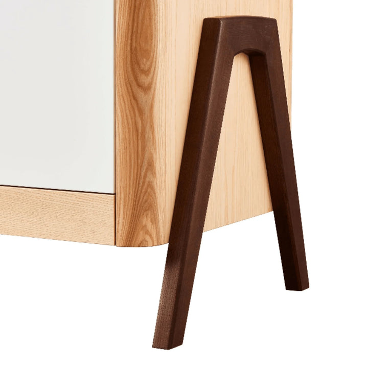 Close-up of the Gaia Baby Hera dresser in Scandi white and natural wood, highlighting the contrasting walnut A-frame leg and smooth rounded corner craftsmanship